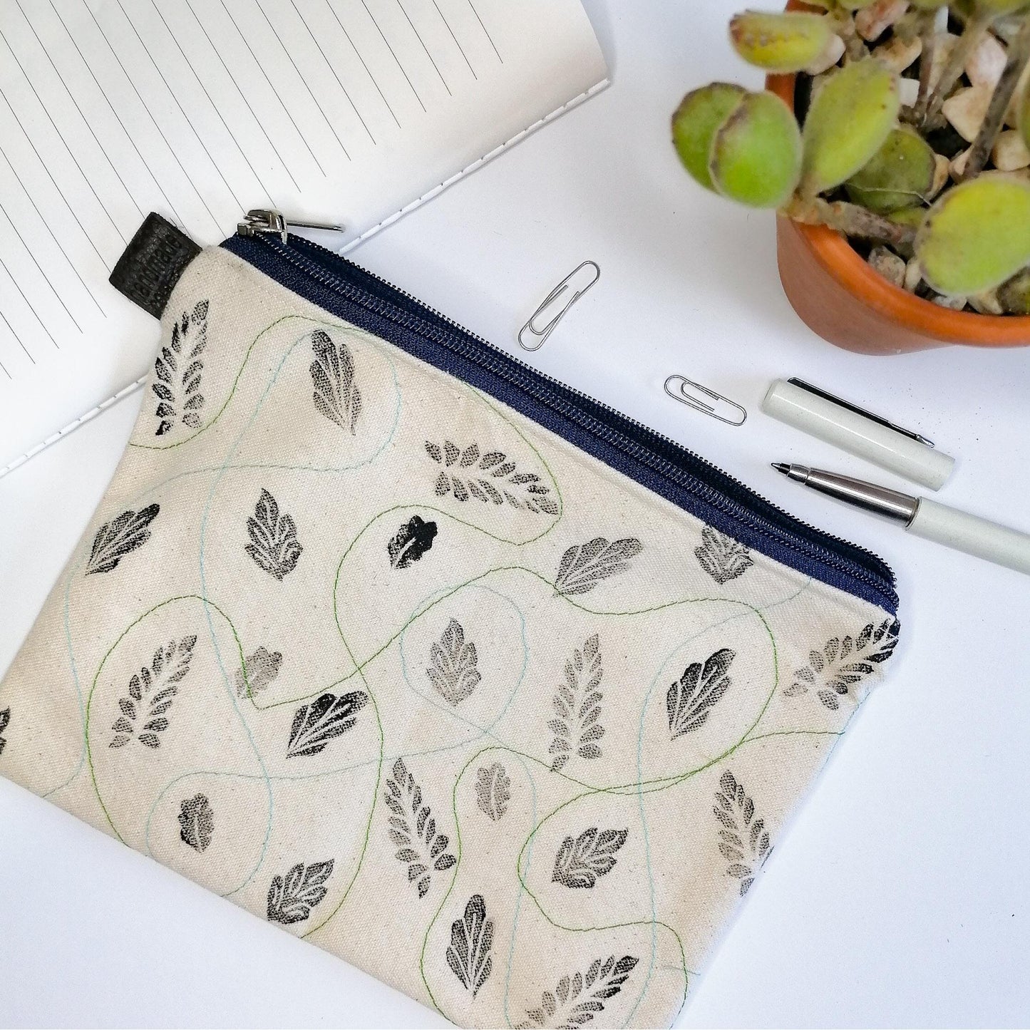 Lined Zipper Cosmetic Bag with handprinted black leaves with blue and green wavy stitches in between. Blue zip. Leather tag.