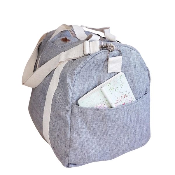 Large Duffel Bag with multiple inner and outer pockets, made with light grey fabric. Cotton webbing handles and adjustable sling. Side view