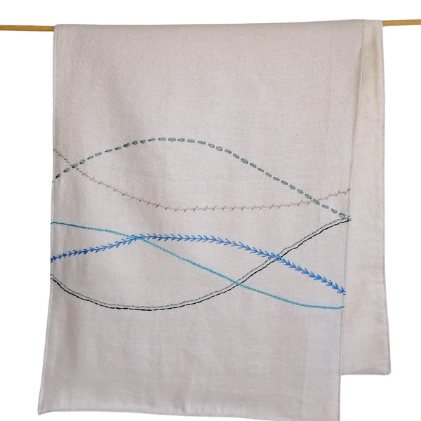 Sand coloured linen table runner with hand embroidered wavy lines in shades of blue.