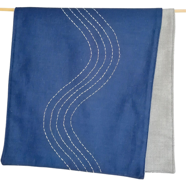Navy coloured linen table runner with hand embroidered slow waves in shades of white.