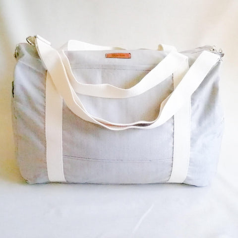 Large Duffel Bag with multiple inner and outer pockets, made with light sand coloured fabric. Cotton webbing handles and adjustable sling. Front view