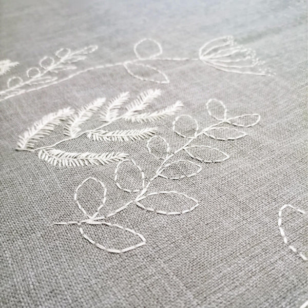 Sage coloured linen table runner with hand embroidered veldt flowers in white. Close up.