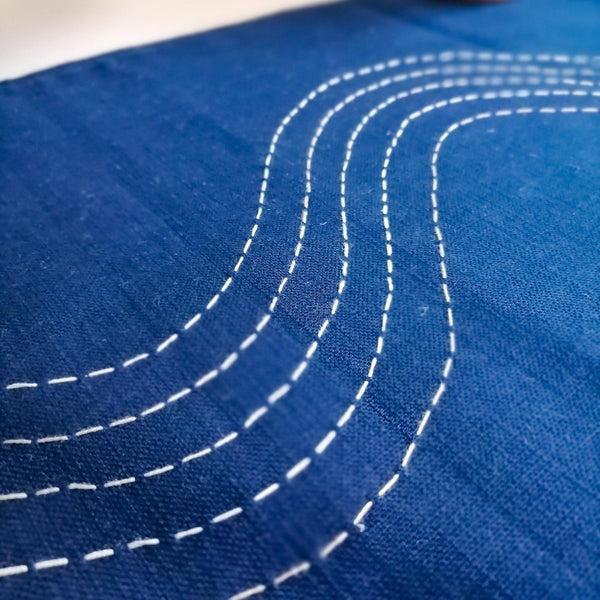 Navy coloured linen table runner with hand embroidered slow waves in shades of white. Close up