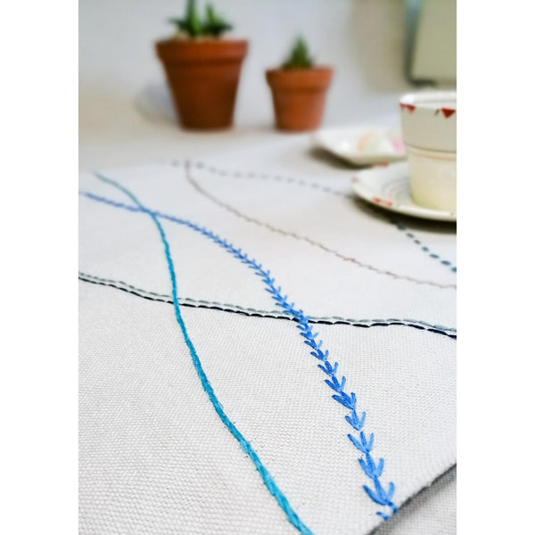 Sand coloured linen table runner with hand embroidered wavy lines in shades of blue.