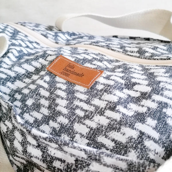 Large Duffel Bag with multiple inner and outer pockets, made with fabric with black & white dimaond motive. Cotton webbing handles and adjustable sling. Close up of fabric