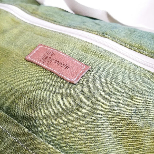 Large Duffel Bag with multiple inner and outer pockets, made with green lightweight denim fabric. Cotton webbing handles and adjustable sling. Close up view of fabric