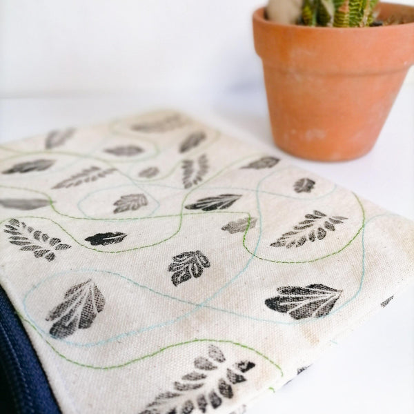Lined Zipper Cosmetic Bag with handprinted black leaves with blue  and green wavy stitches in between. Blue zip. Leather tag. Side view