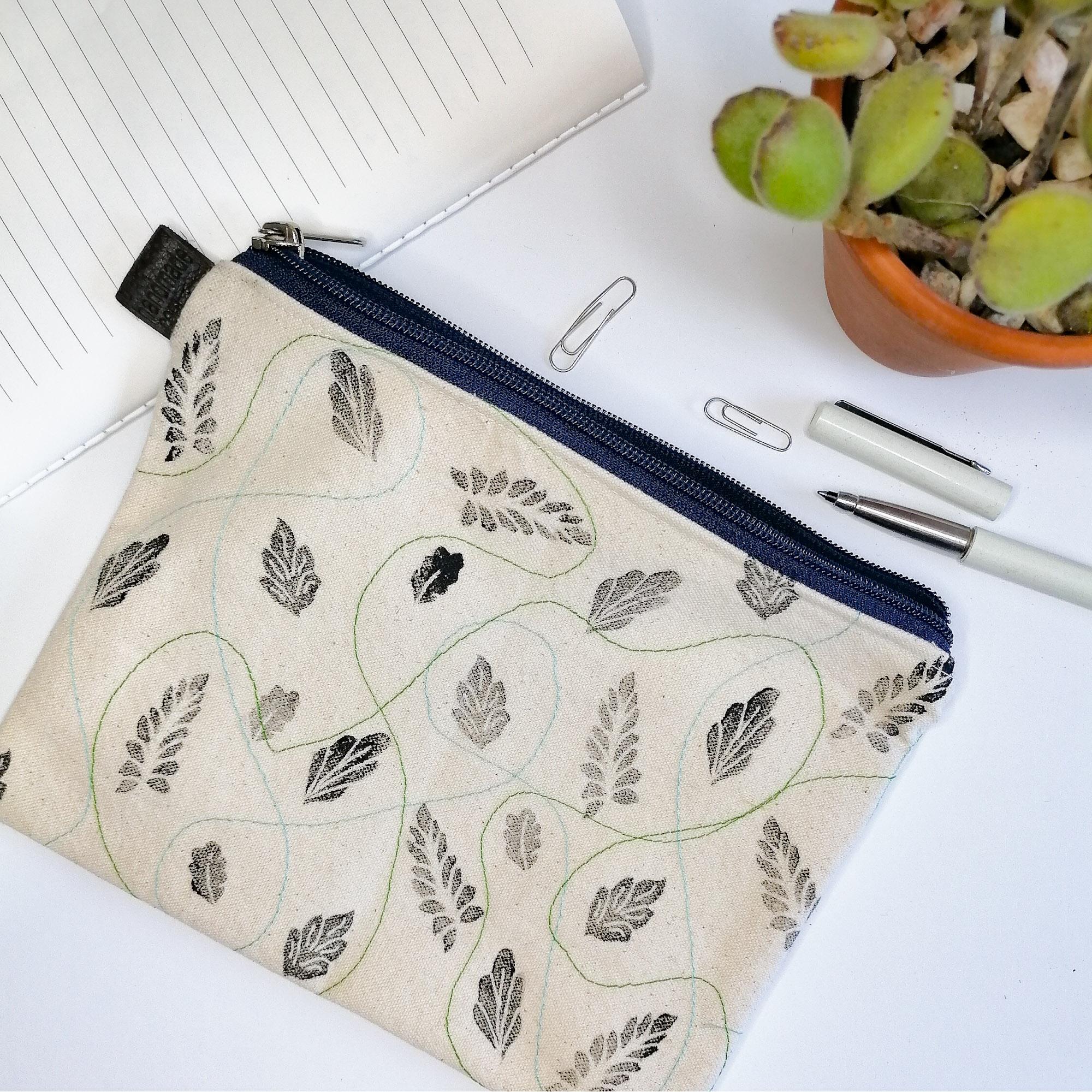 Lined Zipper Cosmetic Bag with handprinted black leaves with blue  and green wavy stitches in between. Blue zip. Leather tag.