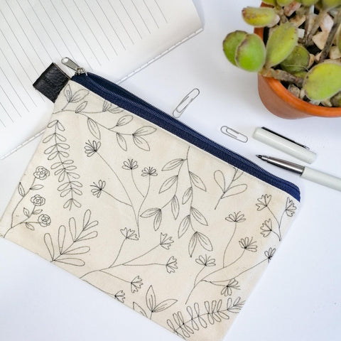Lined Zipper Cosmetic Bag with hand drawn black veldt flowers. Blue zip. Leather tag. Top view.